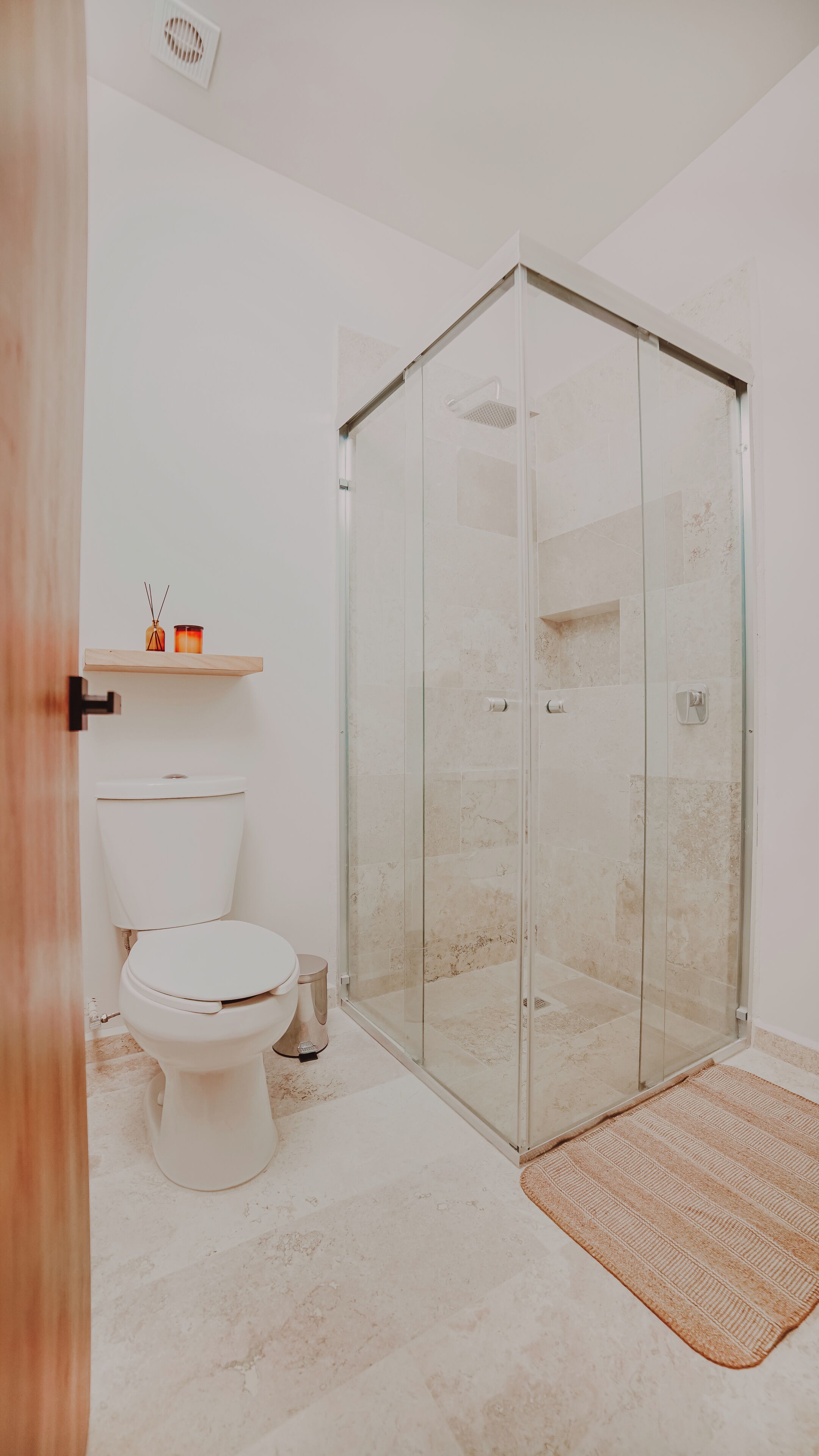 Une salle de bain avec une douche à parois de verre, des toilettes et une petite étagère avec des bougies.
