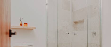 Une salle de bain avec une douche à parois de verre, des toilettes et une petite étagère avec des bougies.