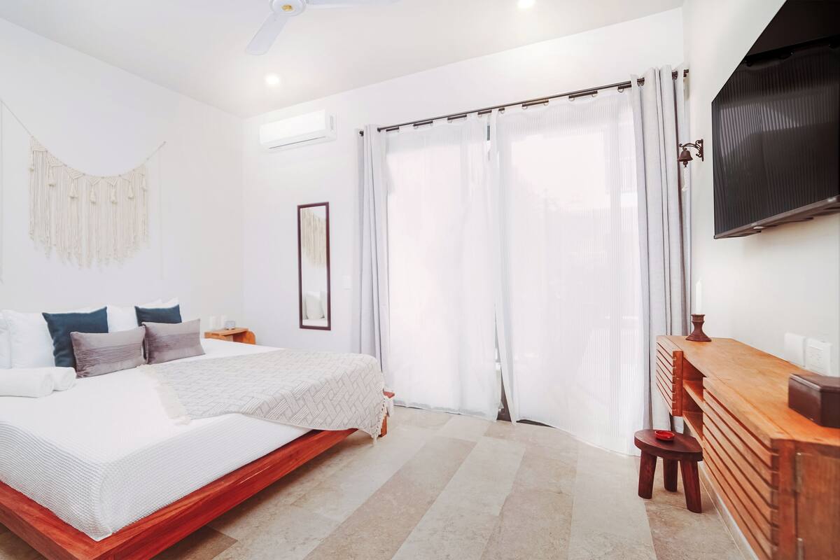 A modern bedroom with a large bed, a wooden dresser, a TV, and a ceiling fan.