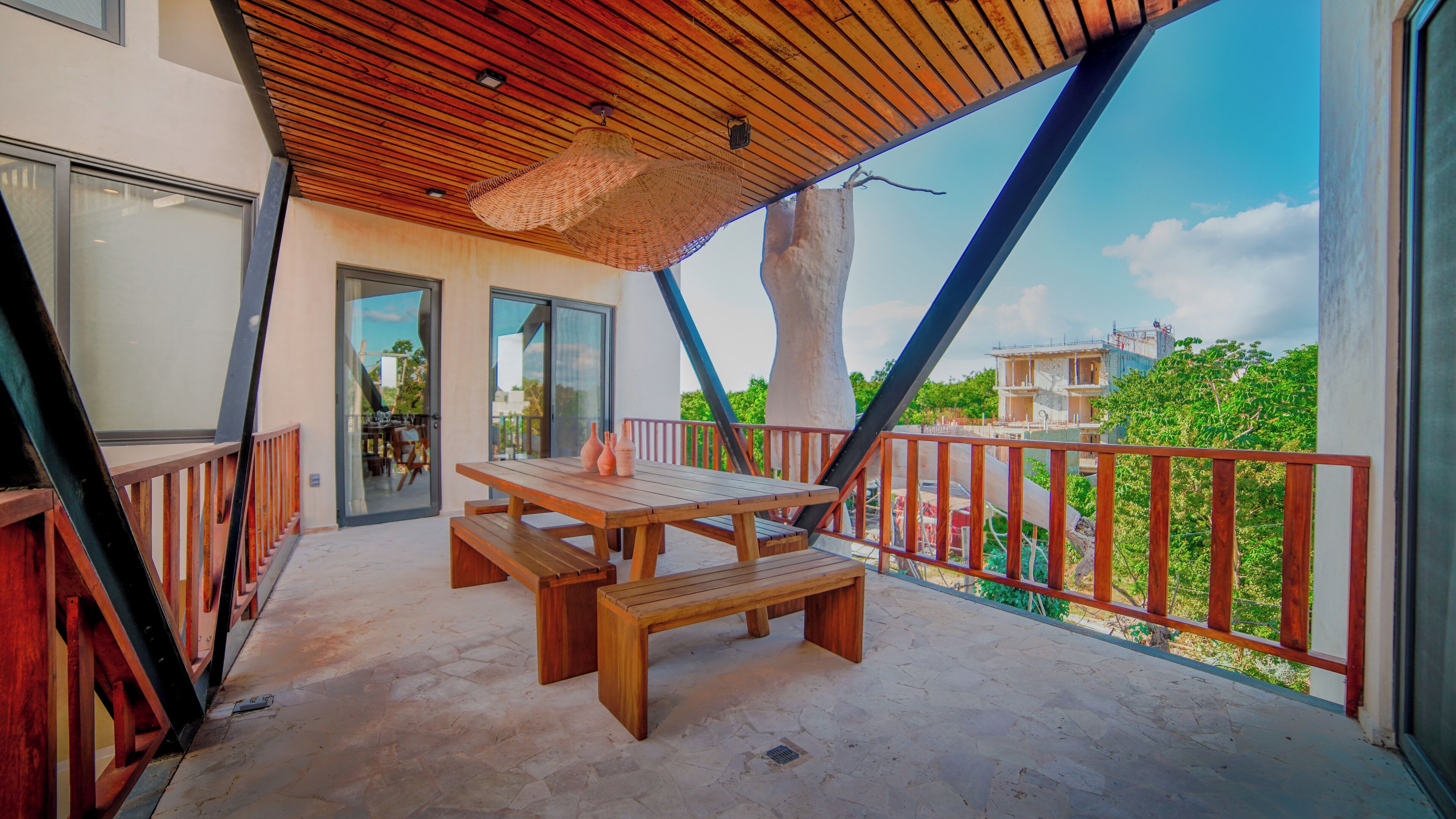 A wooden deck with a table and benches, a glass door leading to an interior space, and a view of a building in the background.