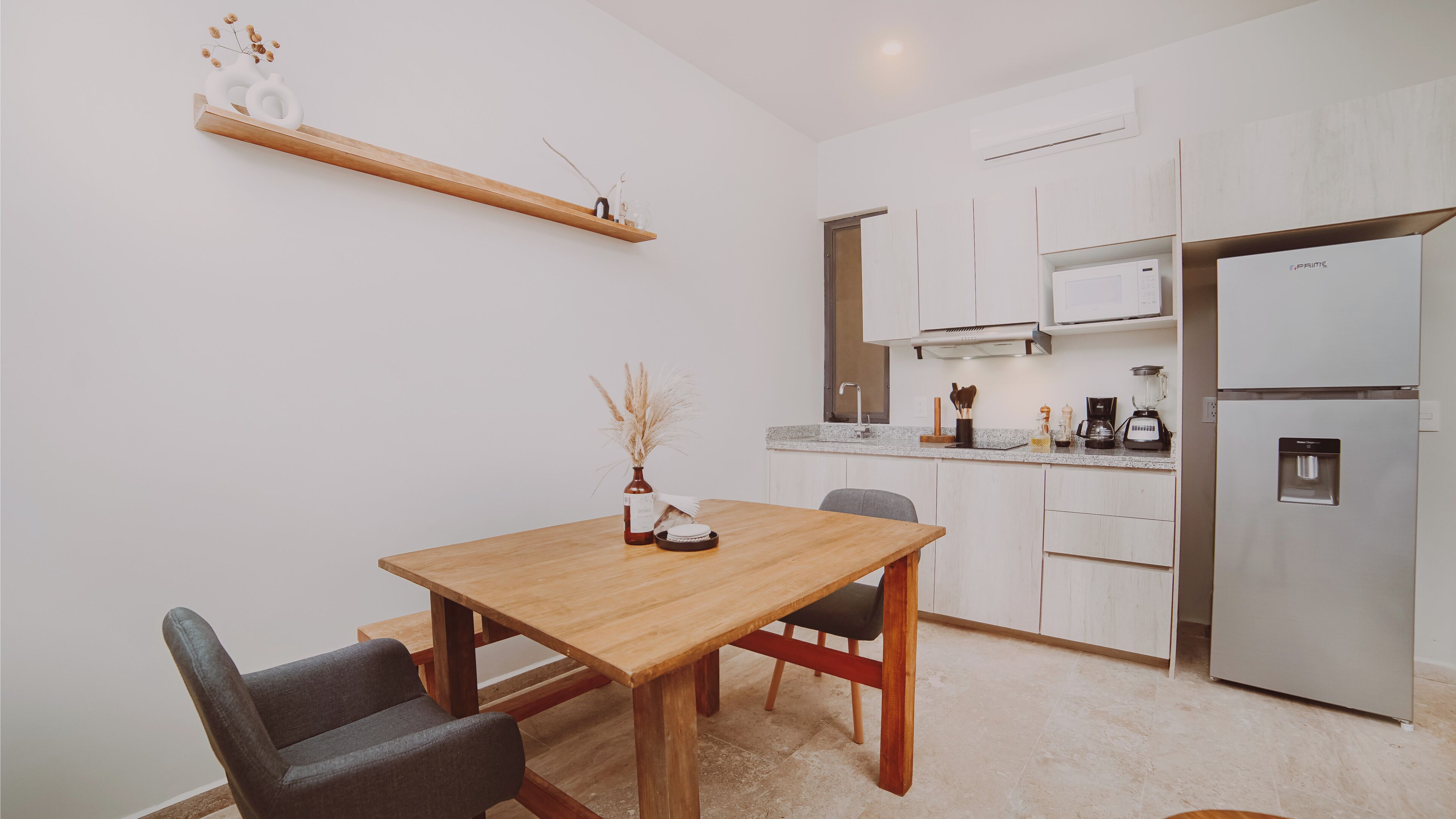 A compact kitchen with a wooden table, chairs, a refrigerator, and a microwave.