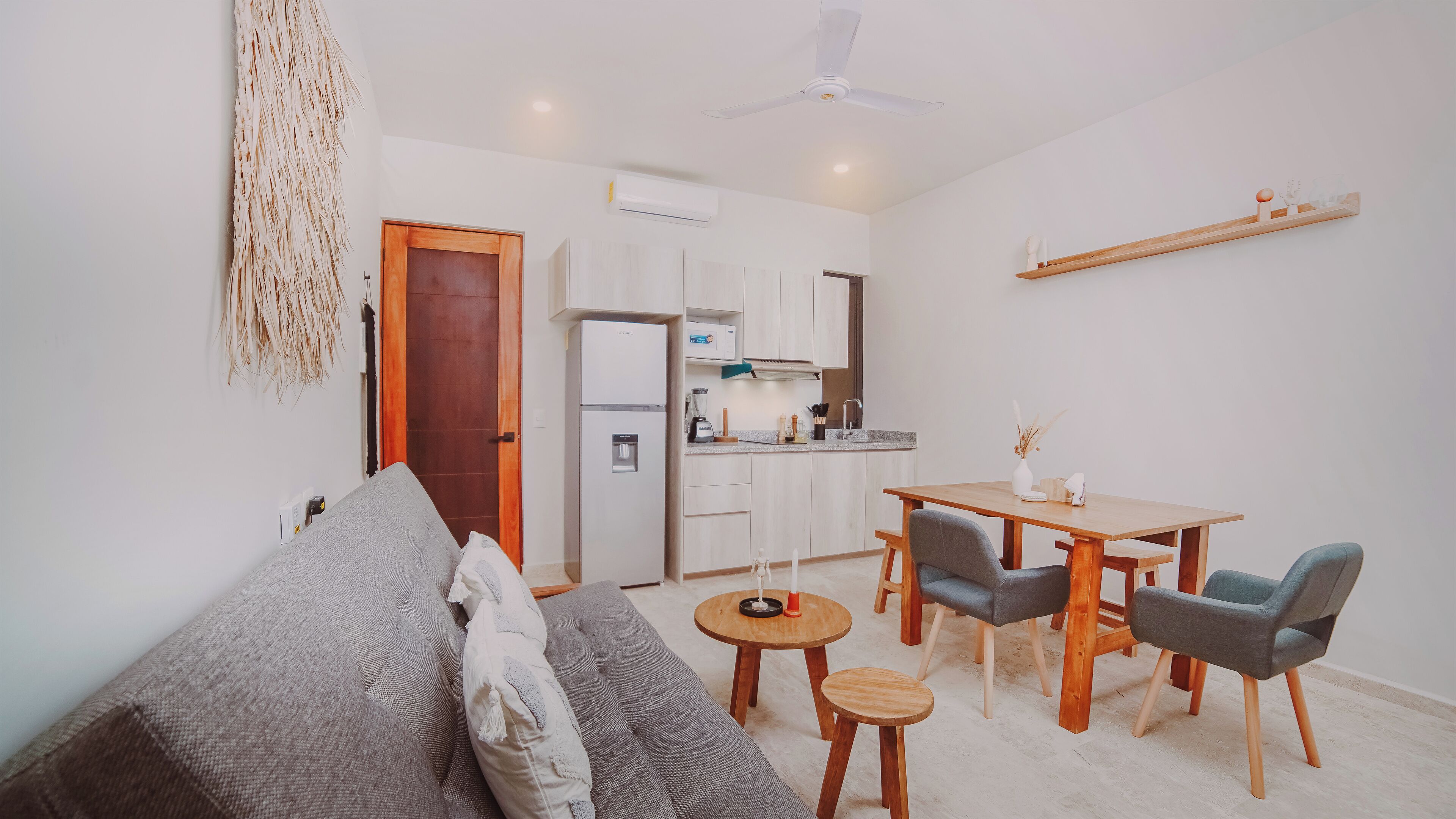 Un salon moderne comprenant un canapé, une table à manger avec des chaises, un coin cuisine et un ventilateur de plafond.