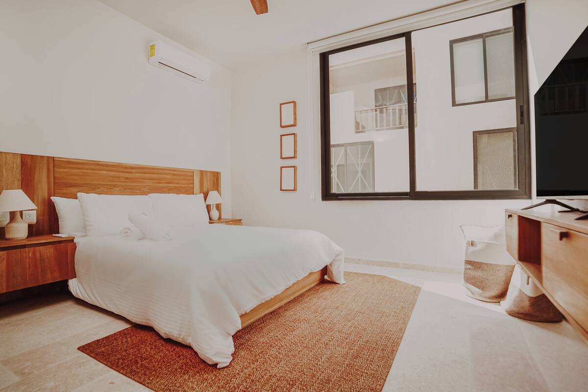 A hotel room with a bed, bedside tables, a TV, a window, and a wooden headboard.