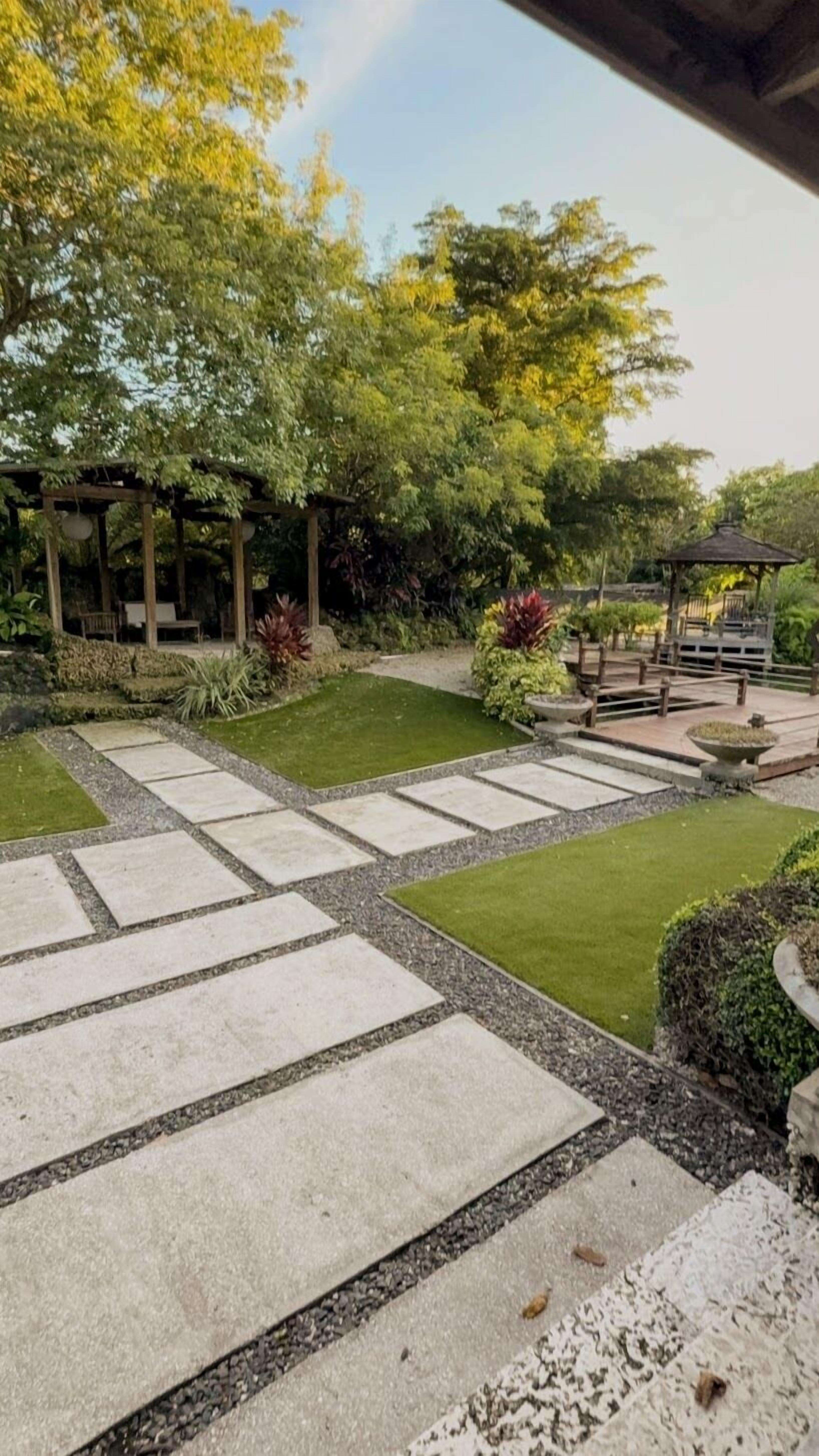 Un jardín con un camino empedrado, una pérgola y un pabellón.