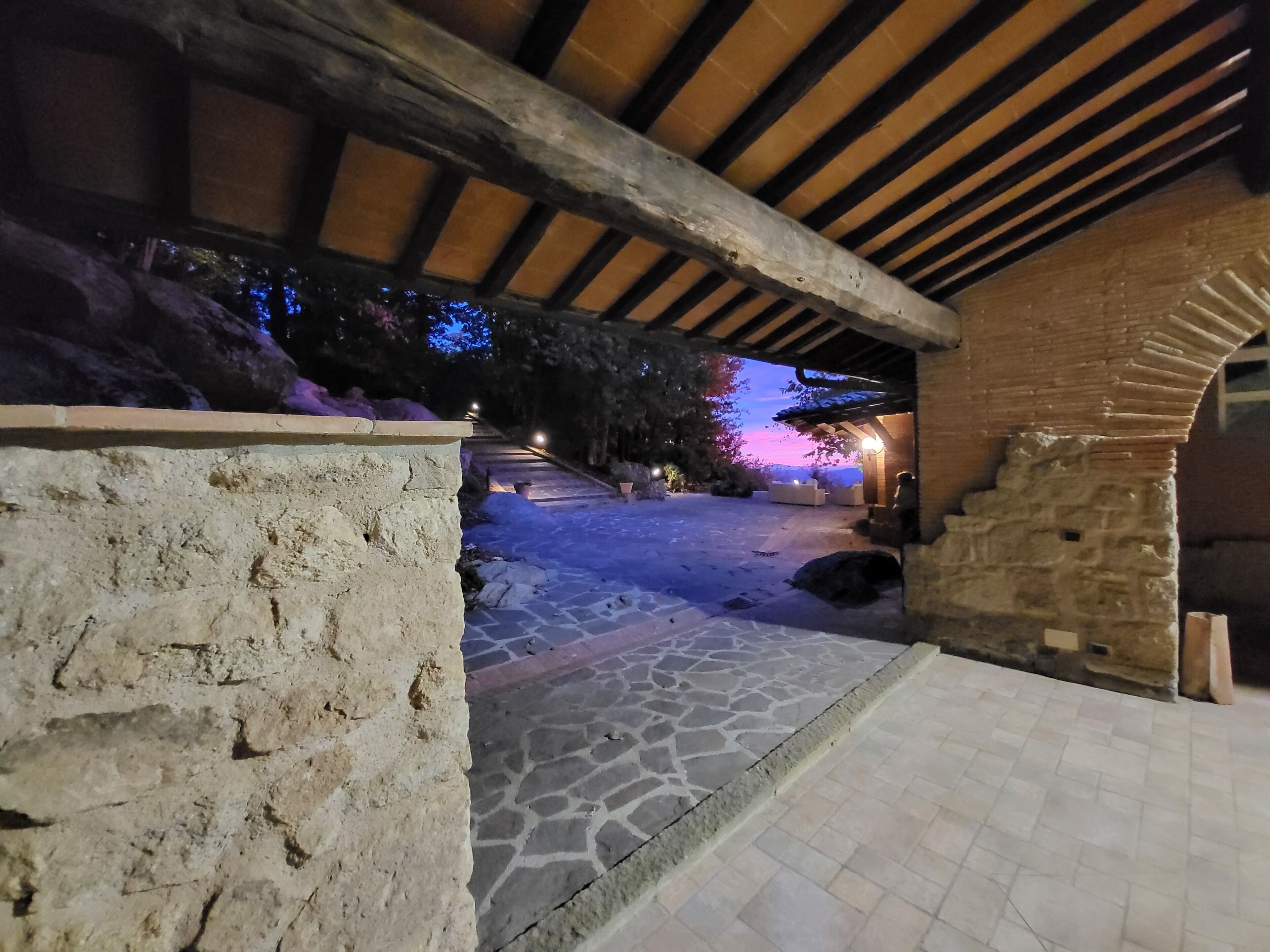 Un chemin de pierre mène à un espace extérieur abrité, doté d’un plafond en bois et de murs en briques.