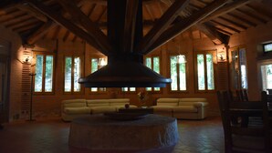Uma sala de estar ampla com lareira de pedra, vigas de madeira e grandes janelas.