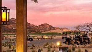 An outdoor dining area with a table set for two, overlooking a desert landscape with golf carts and a distant building. - CONDO Q BY TRVL2HM (Cabo San Lucas)