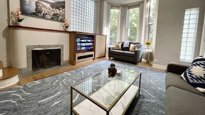 A spacious living room with a fireplace, a large flat-screen TV, a grey sofa, and a marble coffee table.