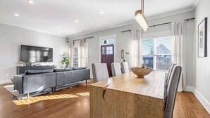 A modern living room with a wooden dining table, grey sofas, and a flat-screen TV. - Pet Friendly Large House | 10 Min to Broadway (Nashville)