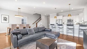 A modern living room with a sectional sofa, a coffee table, and a kitchen area with bar stools. - Pet Friendly Large House | 10 Min to Broadway (Nashville)