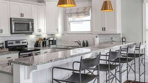 A modern kitchen with white cabinets, stainless steel appliances, a granite countertop, and bar stools. - Pet Friendly Large House | 10 Min to Broadway (Nashville)