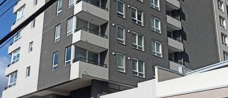 Un edificio residencial de varios pisos con balcones, entrada a nivel de la calle y una puerta de garaje cerrada que dice 'SALA'.