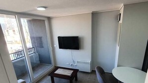 A modern living room with a sofa, a small table, a TV mounted on the wall, and a balcony with a railing. - Apartamentos Bauerle (Temuco)