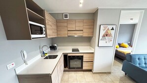 A compact kitchen with built-in appliances, a sink, and a dining area. - Apartamentos Bauerle (Temuco)