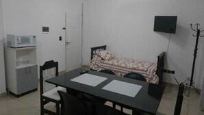 A small, simple room with a bed, a table, chairs, a TV, and a microwave.