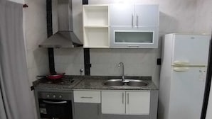 A compact kitchen with a stove, oven, sink, and a white refrigerator.