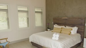 A neatly made bed with white linens and rolled towels, a wooden headboard, and three windows with white blinds. - Perfectly located in Playa Guiones. Walk to the beach, shops, restaurants & yoga (Nosara)