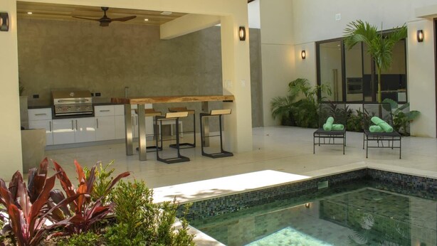 A modern outdoor kitchen with a pool, bar stools, and lounge chairs. - Perfectly located in Playa Guiones. Walk to the beach, shops, restaurants & yoga (Nosara)