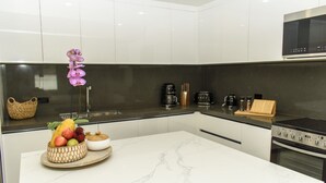 Una cucina moderna con mobili bianchi, un piano di lavoro in marmo, forno integrato e macchina per il caffè.
