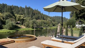 A wooden deck with lounge chairs and a hot tub, overlooking a lake and forested hills. - Boho Manor Resort - Room F (Monte Rio)