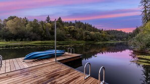 A wooden dock extending into a calm lake with a canoe on it, surrounded by dense trees and a colorful sky. - Boho Manor Resort - Room F (Monte Rio)