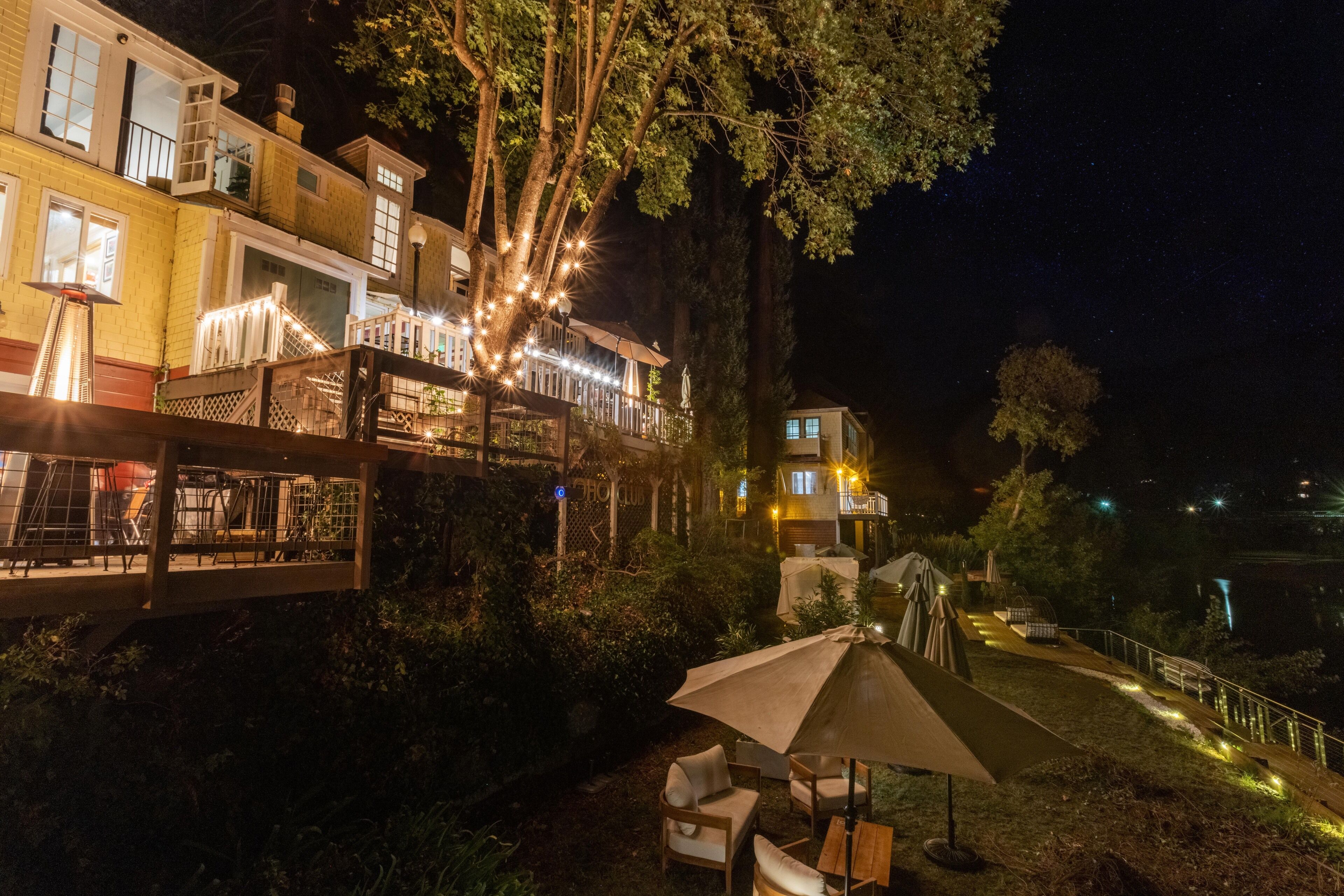 A nighttime view of a hotel with outdoor seating, a staircase, and a well-lit balcony area.