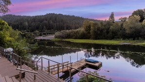 A wooden deck with a dock extending over a calm lake, surrounded by dense forest and a clear sky. - Boho Manor Resort - Room 28 (Monte Rio)