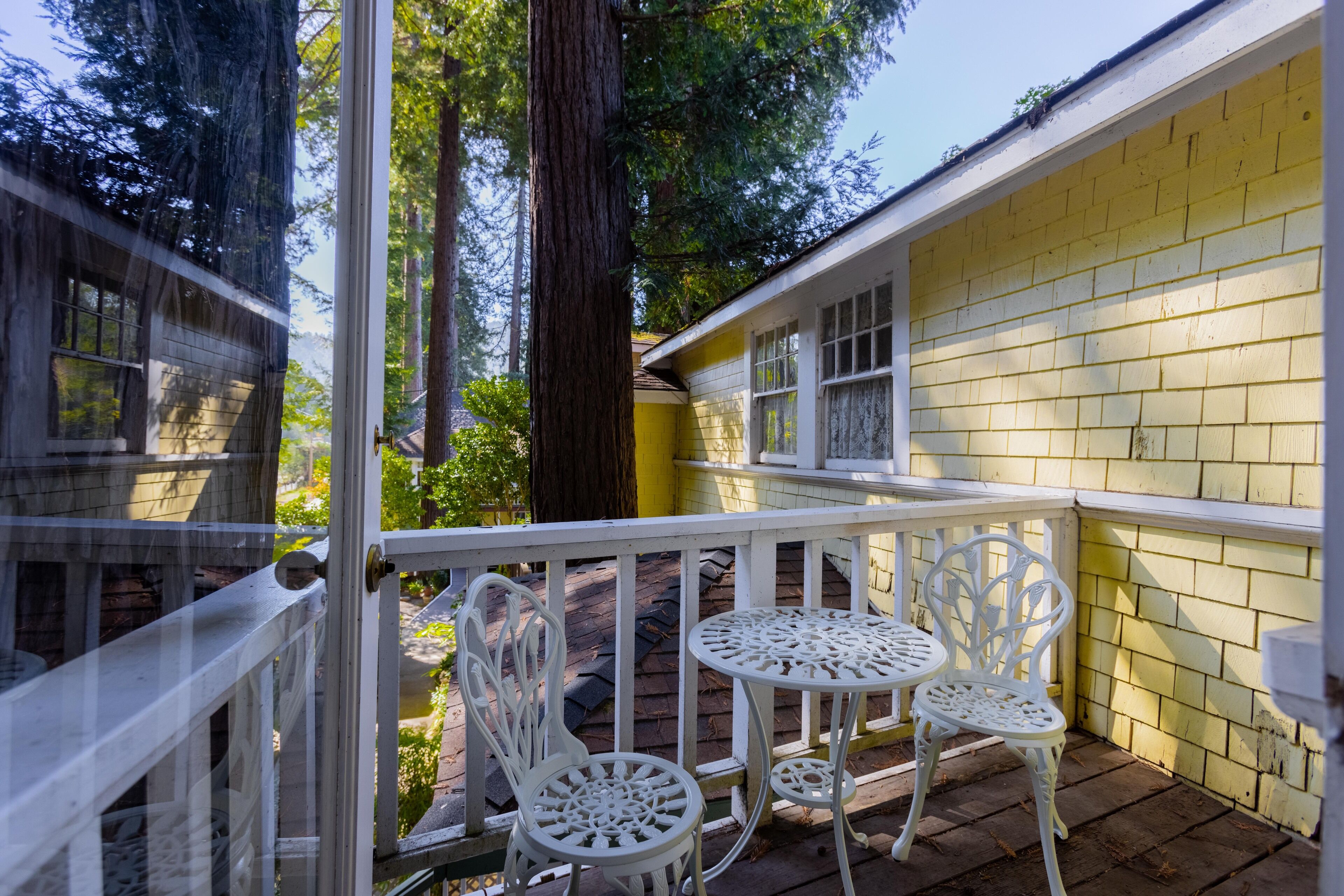 A covered outdoor area with a white railing, two white metal chairs, and a small table.