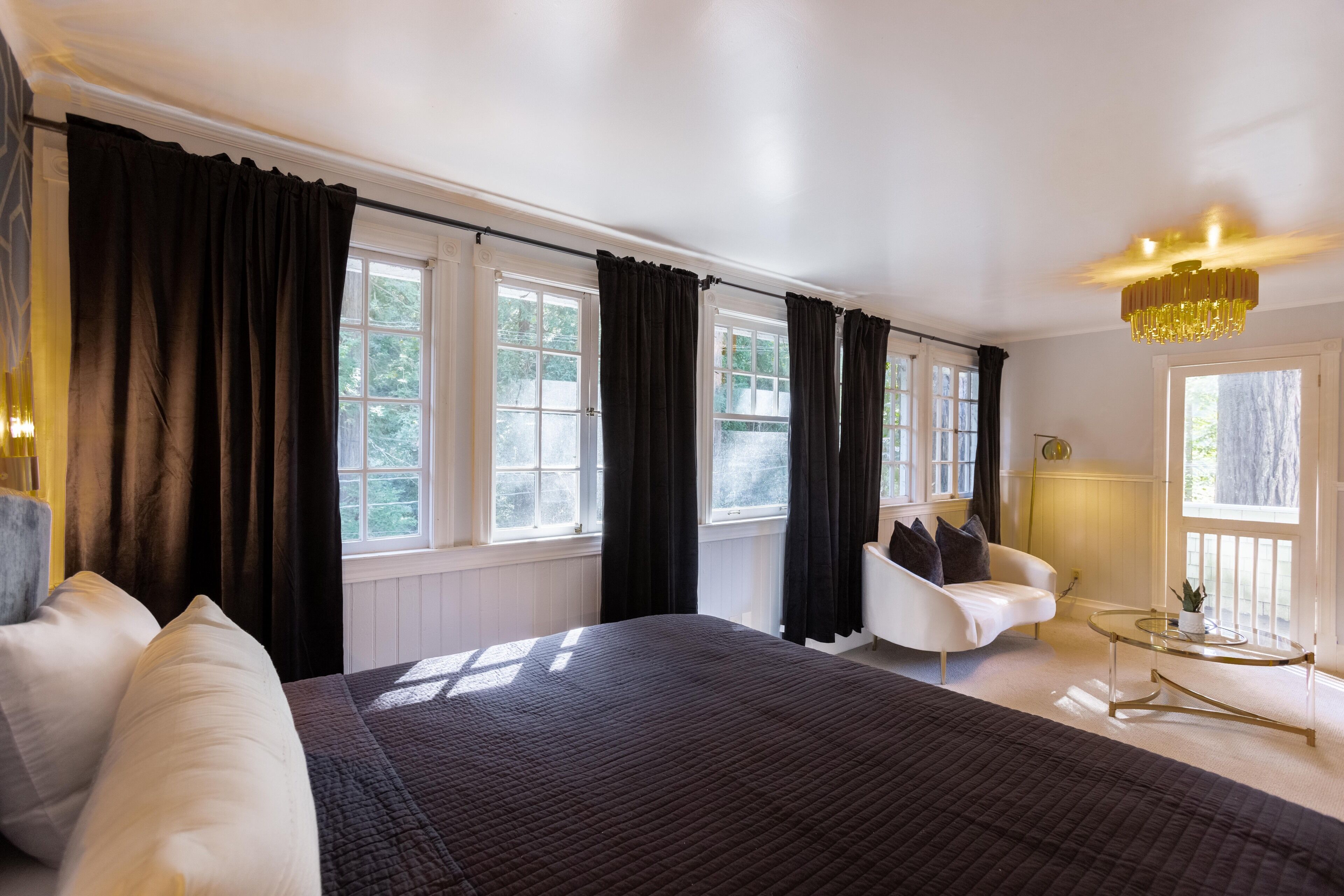 A bedroom with a large bed, a white armchair, a glass coffee table, and a chandelier.