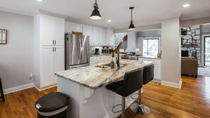 A modern kitchen with white cabinetry, stainless steel appliances, and a marble island with bar stools.