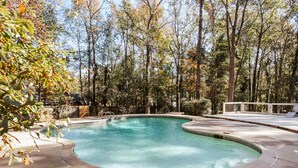 A swimming pool with a curved edge, surrounded by a concrete deck and trees.