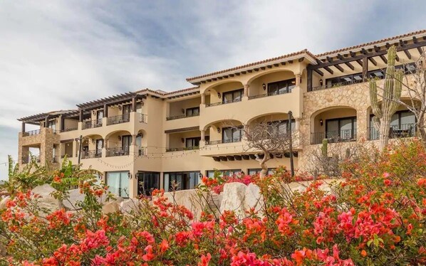 Un hôtel à plusieurs étages, doté de balcons, d’une façade en pierre et d’un jardin agrémenté de fleurs rouges.