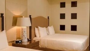 A hotel room with two beds, a ceiling fan, a nightstand with a lamp, and a wall with square cutouts. - CONDO A BY TRVL2HM (Cabo San Lucas)