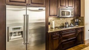 A kitchen with stainless steel appliances, dark wooden cabinets, and a granite countertop. - CONDO A BY TRVL2HM (Cabo San Lucas)