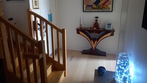 Een trap leidt naar een plateau met een houten leuning. Op het plateau staat een bureau met een decoratieve vaas en een klein beeldje. Daarboven hangt een kleurrijk abstract schilderij aan de muur.