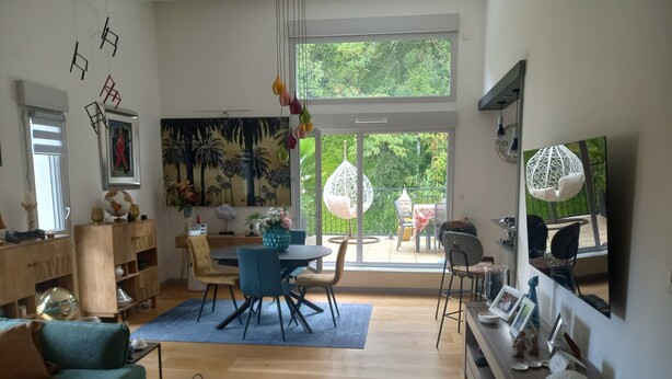 Een moderne woonkamer met een eethoek, grote ramen en uitzicht op groen.