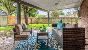 An outdoor patio with a covered seating area, a table with bottles, and a patterned rug.