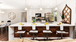 A modern kitchen with white cabinets, a central island with bar stools, and pendant lighting.