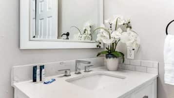 Une salle de bain avec un lavabo blanc, deux robinets, un miroir et une orchidée en pot.