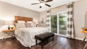 A bedroom with a bed, a bench, a ceiling fan, a nightstand, and a window with curtains.