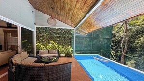 Un espacio exterior moderno con piscina, mobiliario de mimbre y vistas a la vegetación circundante.