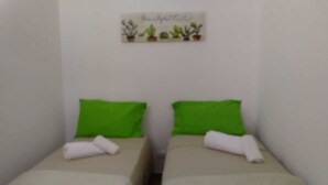 Une petite chambre simple, avec deux lits, chacun agrémenté d’un oreiller vert et d’une serviette blanche. Un petit élément décoratif orne le mur au-dessus des lits.