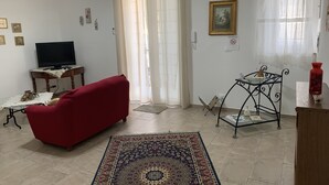Un salon avec un canapé rouge, un téléviseur posé sur une table en bois, un tapis à motifs et une table en métal sur laquelle se trouve un vase.