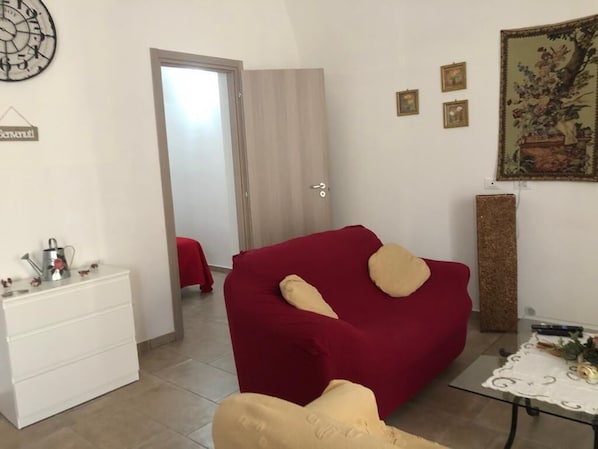 A compact living space with a red sofa, a small white dresser, and a table with a lace tablecloth.