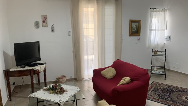 Un salon comprenant un canapé rouge, un canapé beige, une table basse en verre agrémentée d’un arrangement floral, un téléviseur posé sur une table en bois et une étagère en verre ornée d’objets décoratifs.