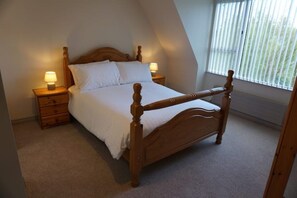 A bedroom with a wooden bed, two bedside tables with lamps, a window with blinds, and a sloped ceiling.