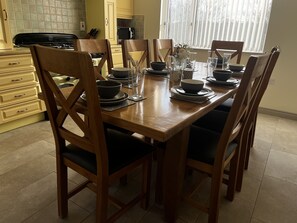 A dining table set with bowls, glasses, and cutlery in a kitchen with wooden chairs and cabinets.