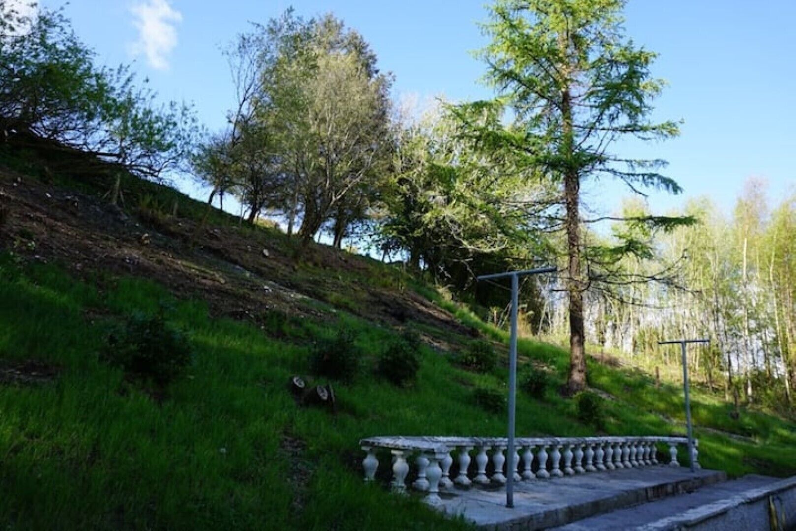 Une balustrade en pierre avec une rampe métallique, une pente herbeuse et des arbres en arrière-plan.