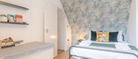 Een slaapkamer met een bed, nachtkastje en een plank met boeken.