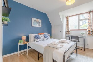 Une chambre à coucher comprenant un lit, un bureau, une chaise, une fenêtre avec des rideaux et un tableau accroché au mur.